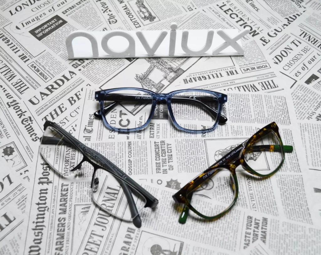 Tres gafas de lectura Naviux de diferentes colores sobre fondo de periódicos con el logo de la marca naviux